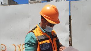 עובד עם קסדה ואפוד זוהר ממלא טופס באתר עבודה